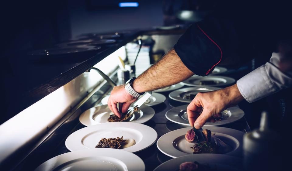 Chefs plating dishes on a service pass in a dark kitchen